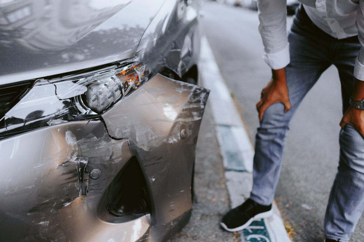 Man inspecting a car with front-end damage parked on the side of the road.