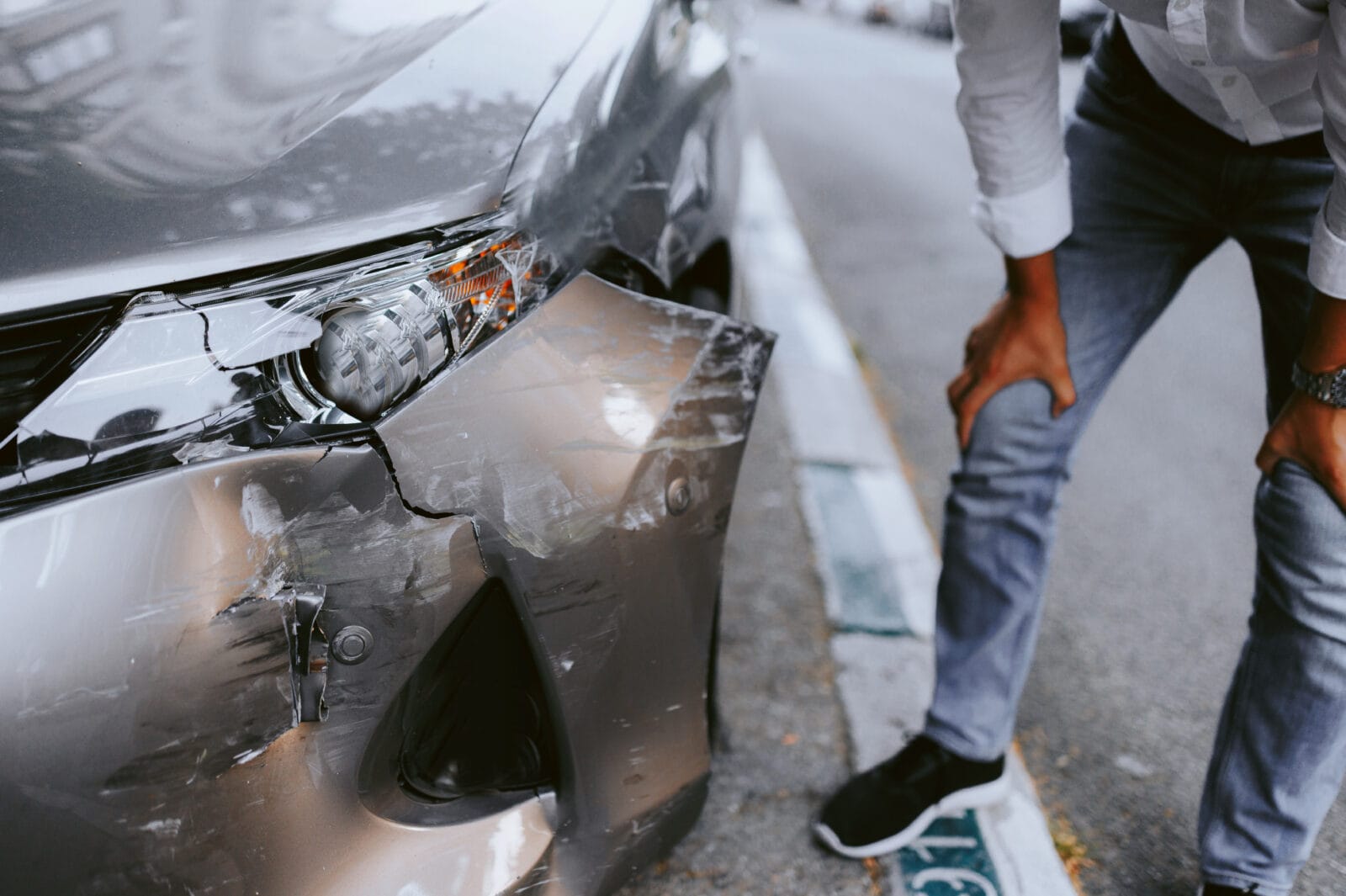 Man inspecting a car with front-end damage parked on the side of the road.
