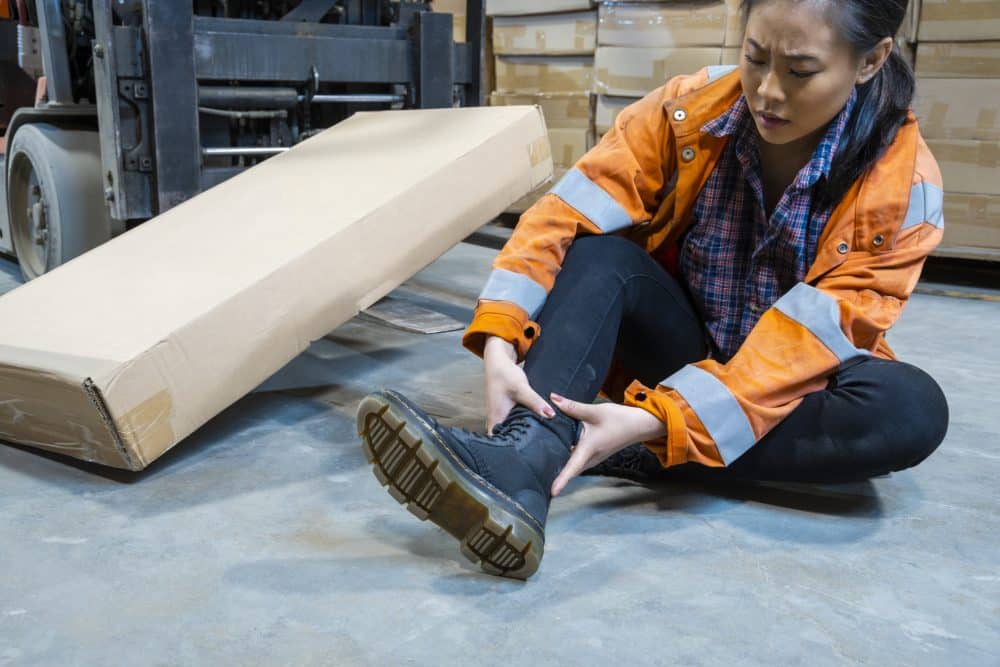 An injured warehouse worker holding her ankle in pain.