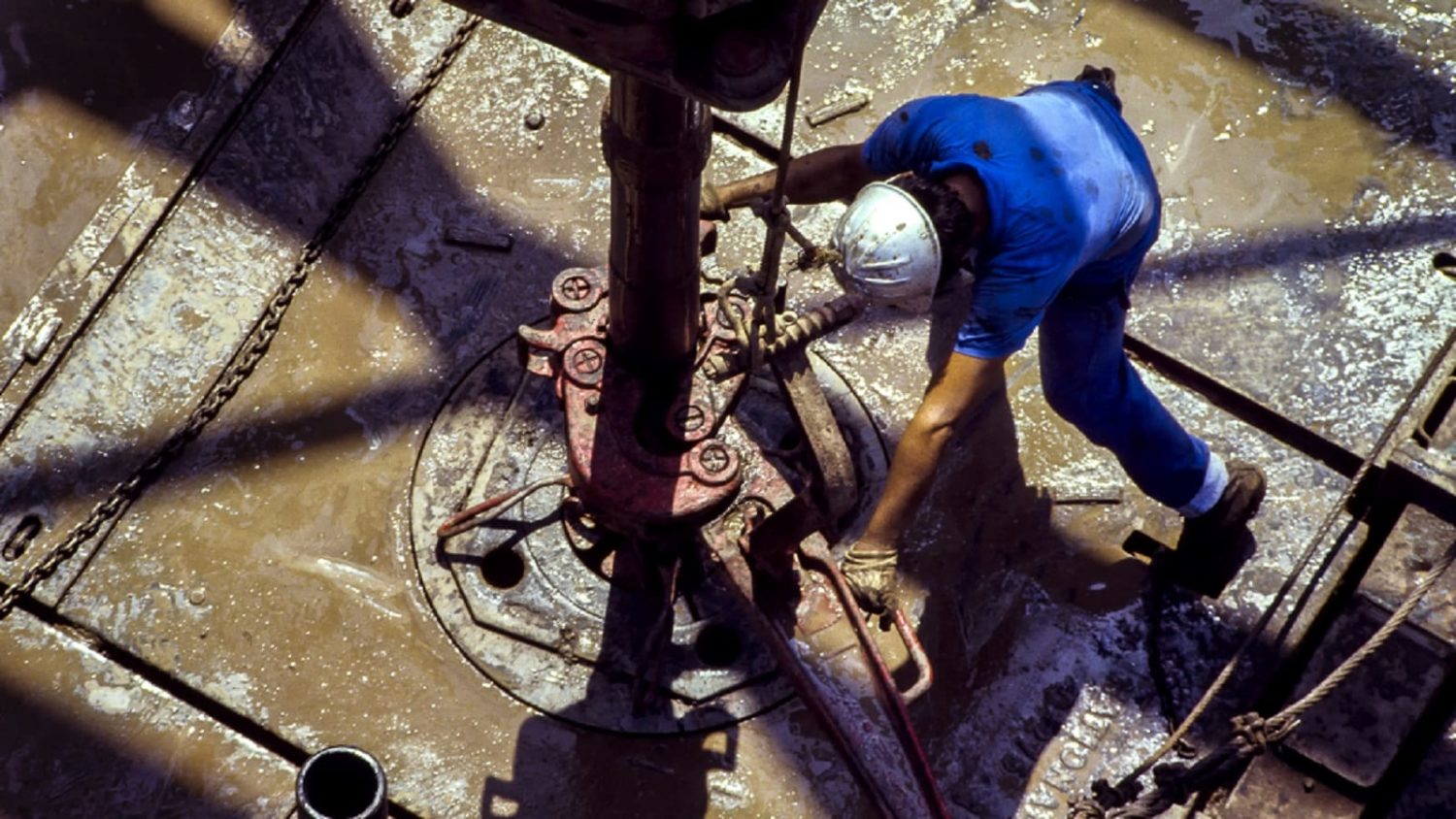 Worker in safety gear operating heavy machinery on an oil rig platform.