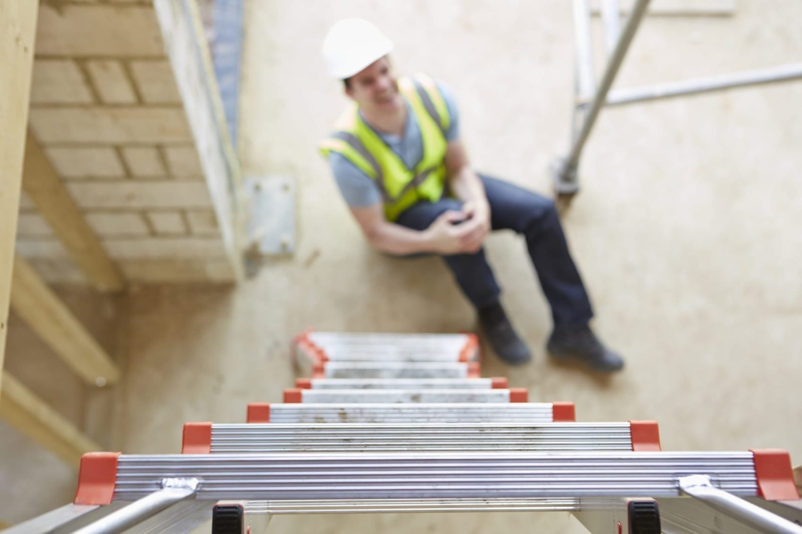 A worker sitting on the ground and holding their knee in pain after falling from a ladder.
