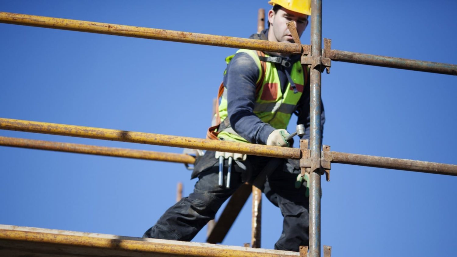 Construction worker in safety gear working on scaffolding.