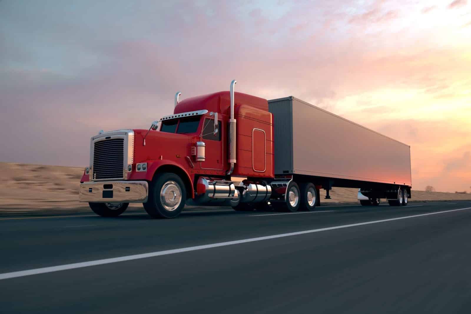 A red semi-truck with a large trailer driving on a highway at sunset.