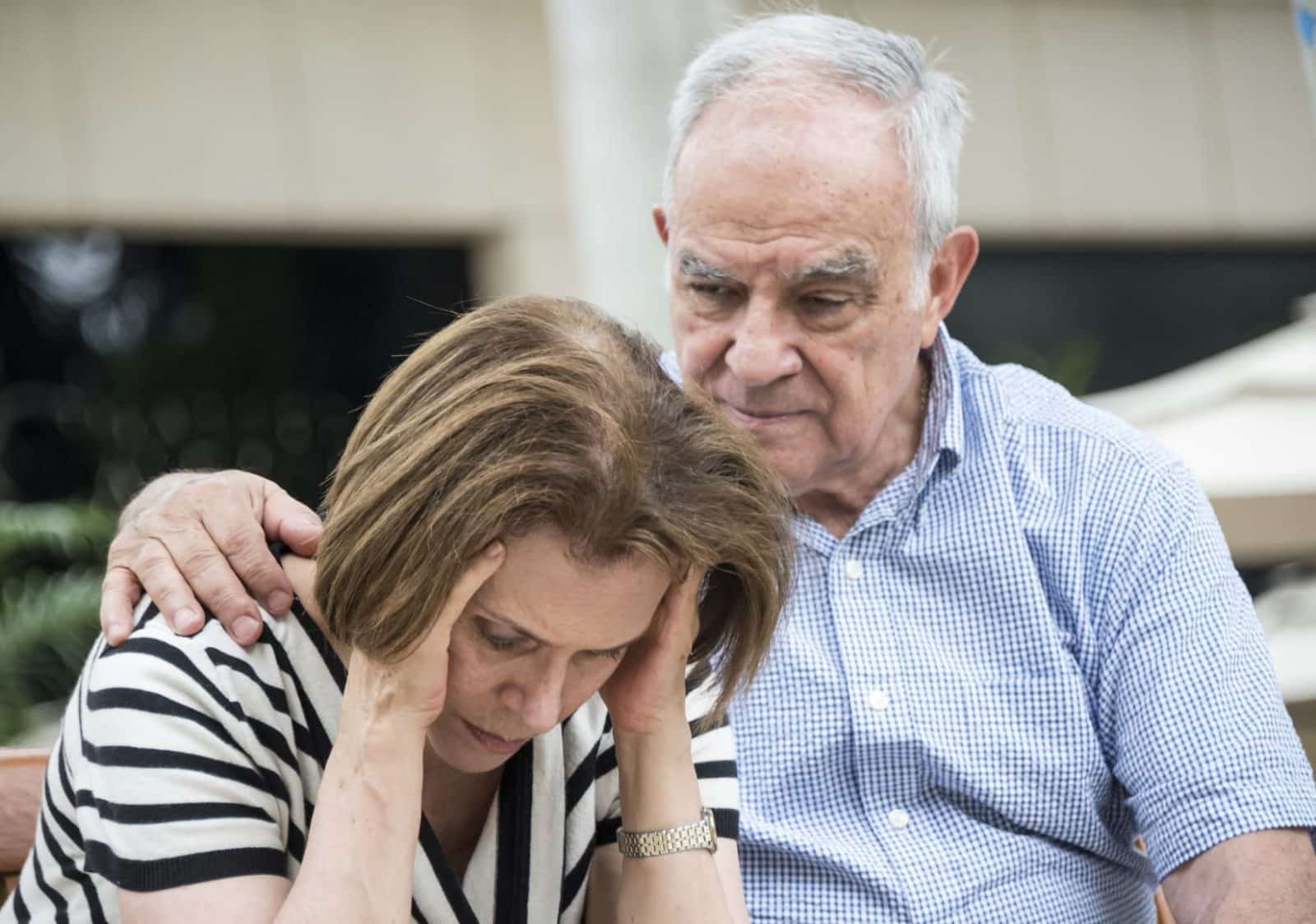 An elderly man comforts a distressed woman who is holding her head in her hands.