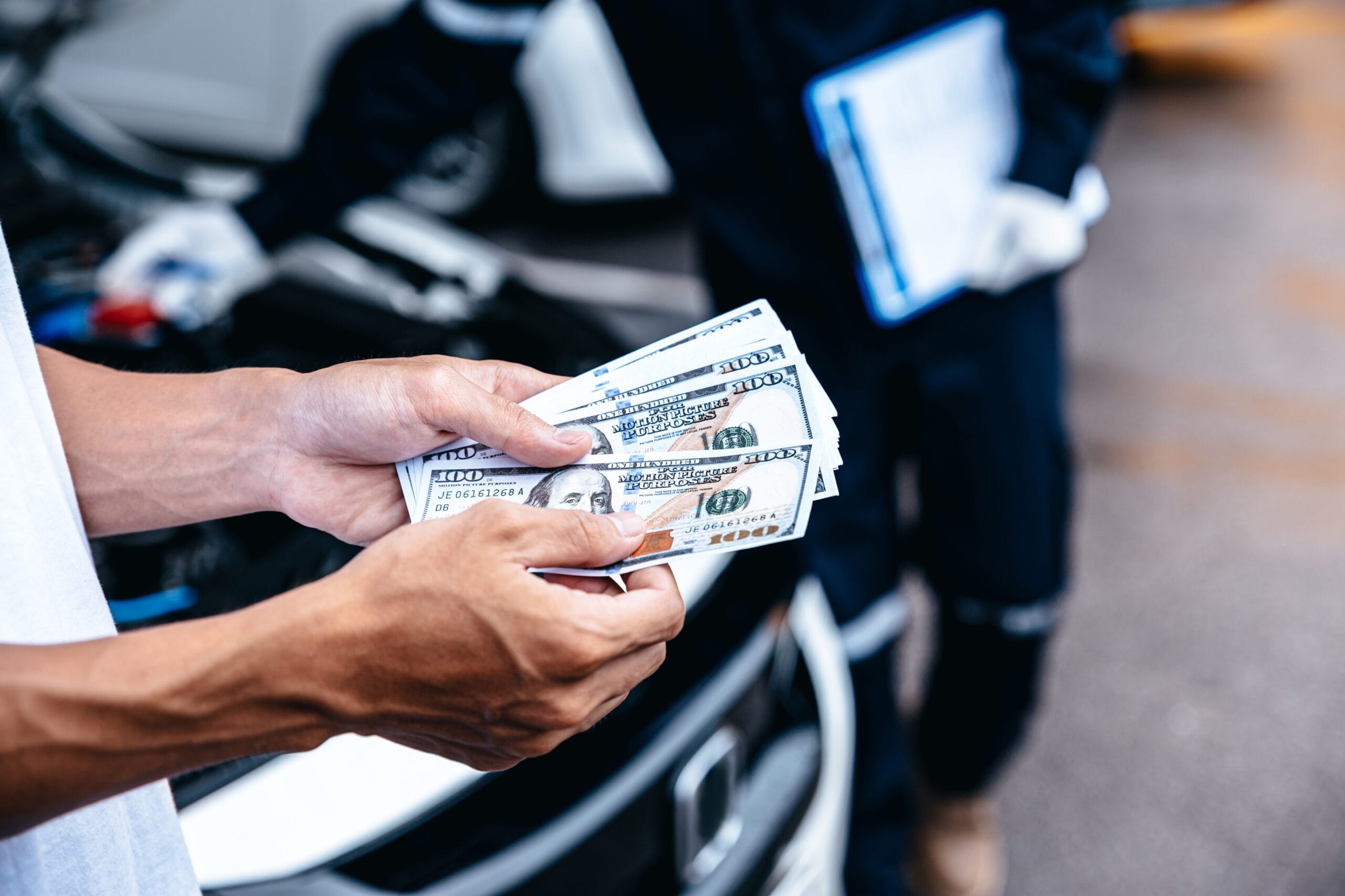 Person holding a stack of hundred-dollar bills in front of a damaged car.