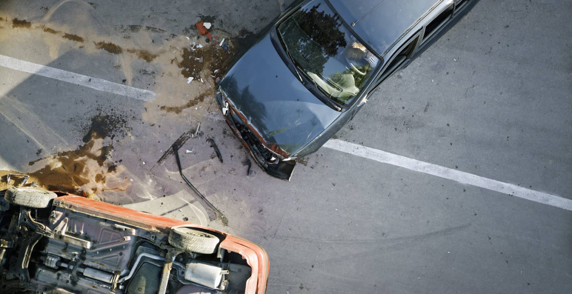 Aerial view of a car accident showing one vehicle flipped on its side and another damaged on the road.
