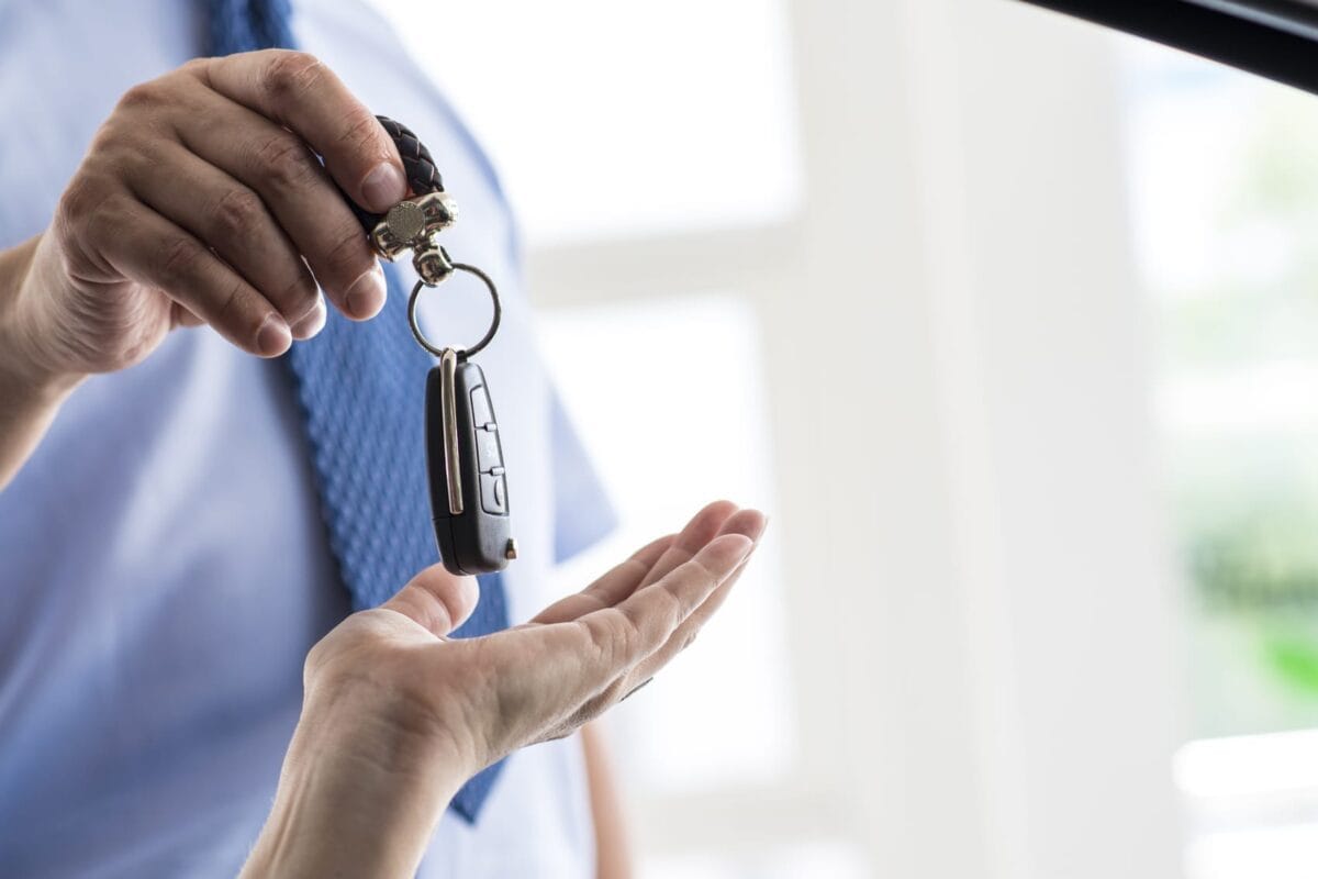 Car salesman handing over a key fob to a customer inside a dealership.