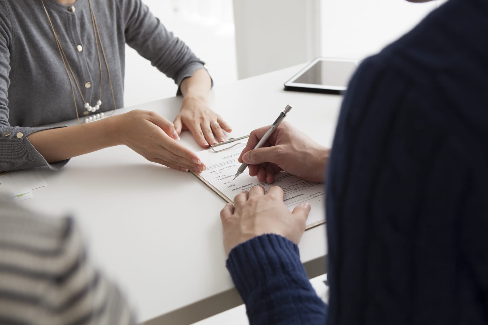 Close-up of two people sitting at a desk, with one person signing paperwork on a clipboard.