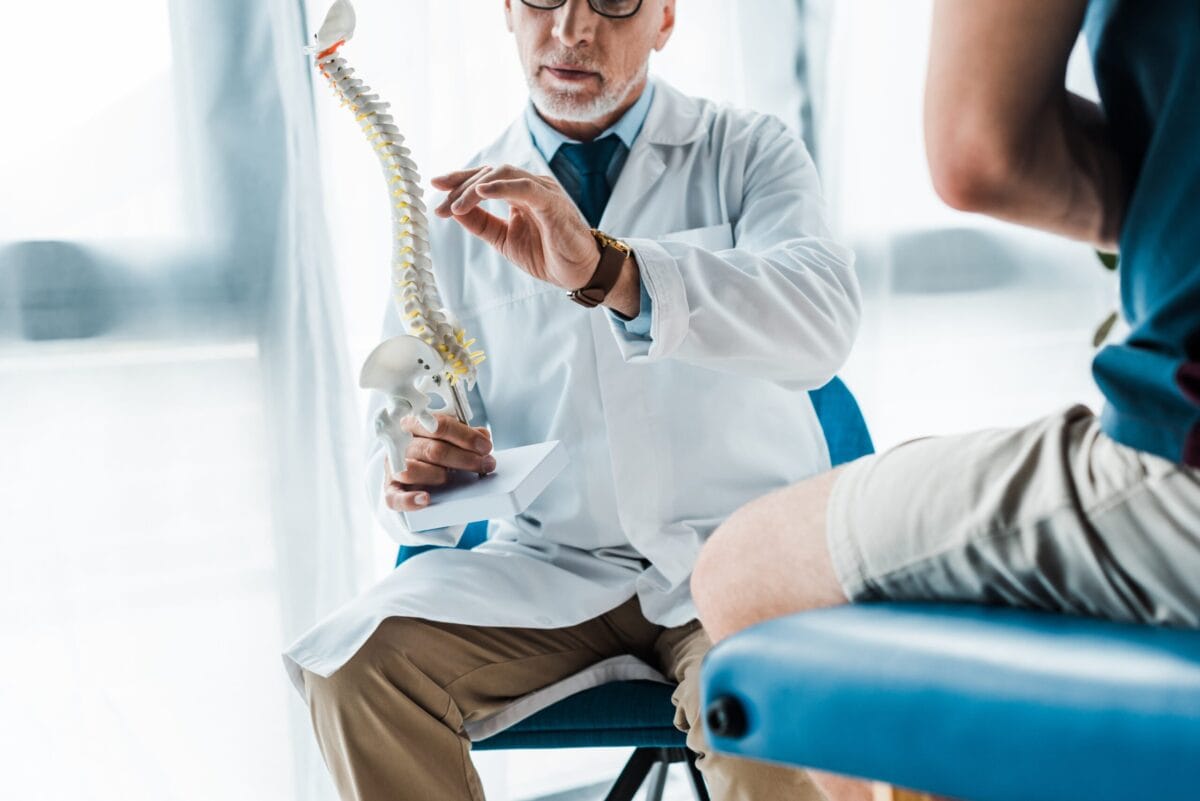 A doctor holding and explaining a spinal model to a patient.