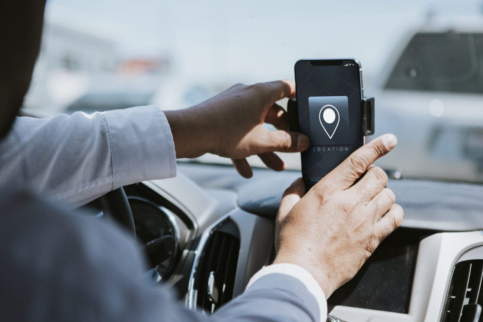 A driver in a car adjusting a smartphone mounted on the dashboard and using a navigation app.