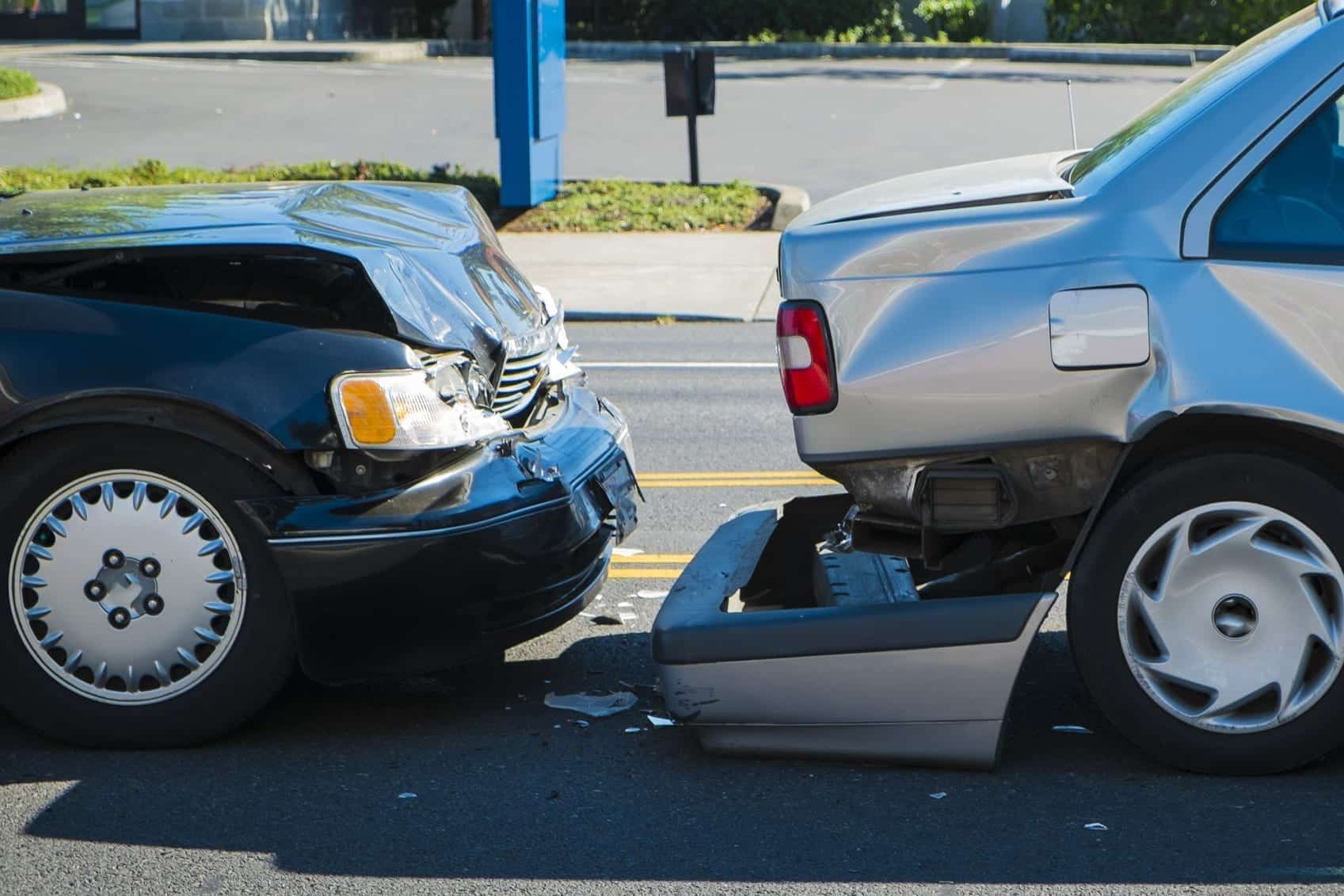 Two cars involved in a rear-end collision, with the front of a black car damaged after hitting the back of a silver car.