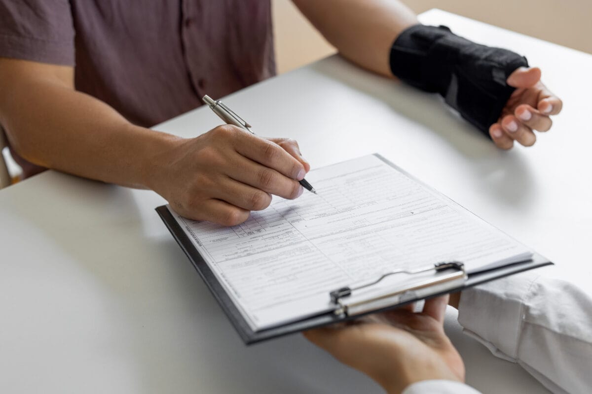 A person with a wrist injury wearing a black brace fills out paperwork on a clipboard.
