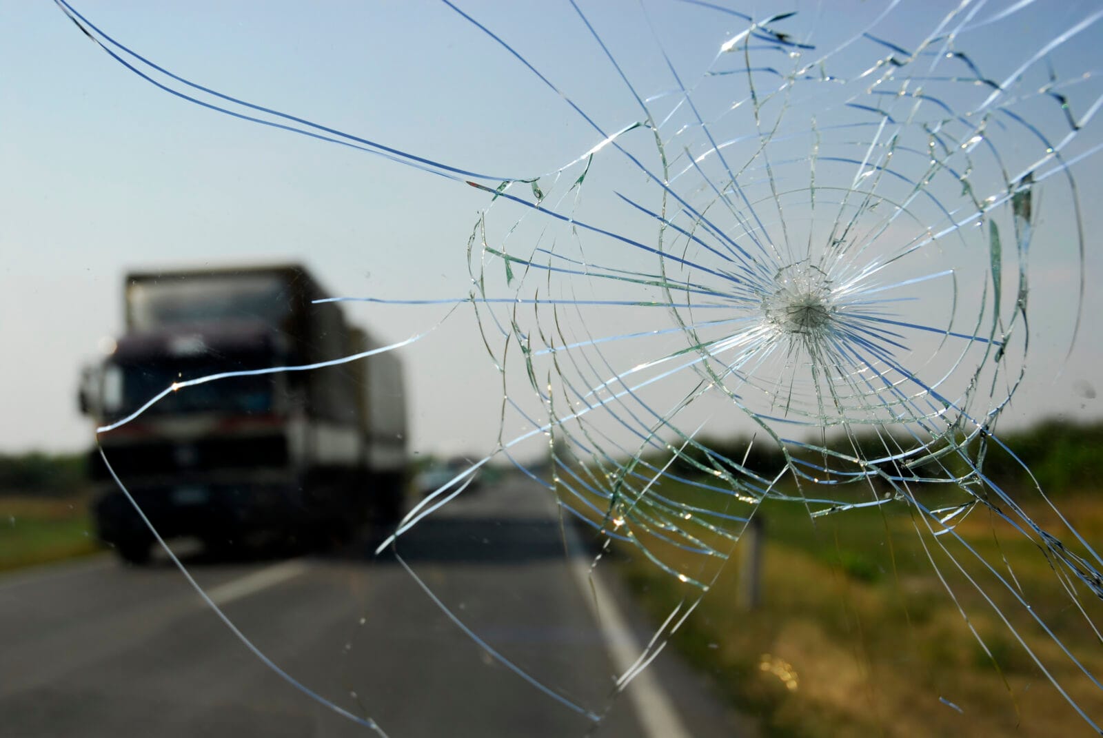 Cracked windshield with a large commercial truck on a highway blurred in the background.