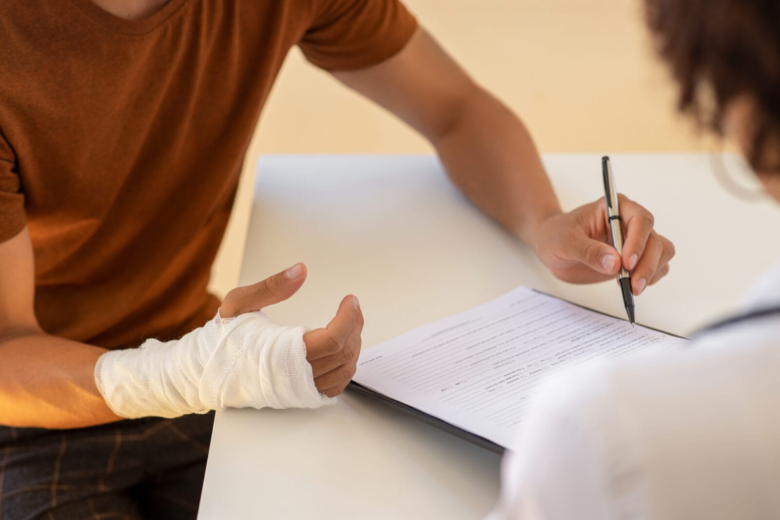 Person with a bandaged wrist signing paperwork at a desk.