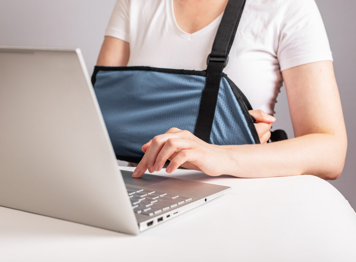 Person wearing an arm sling types on a laptop at a desk.